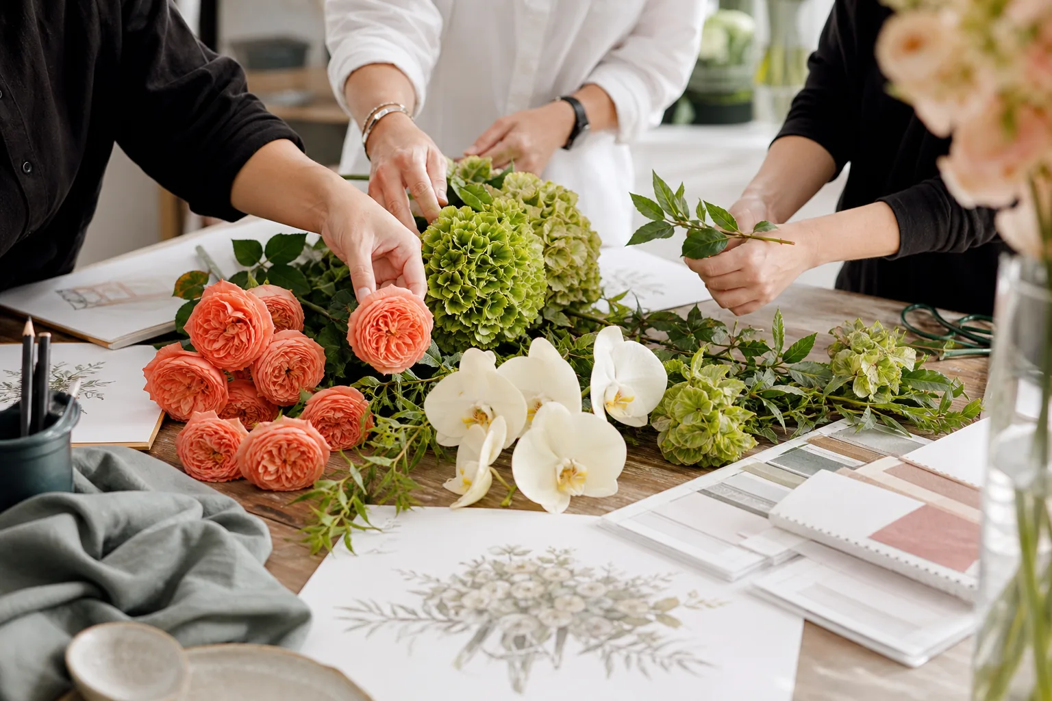 Floral designers collaborating over coral roses, chartreuse hydrangea, orchids, and event sketches